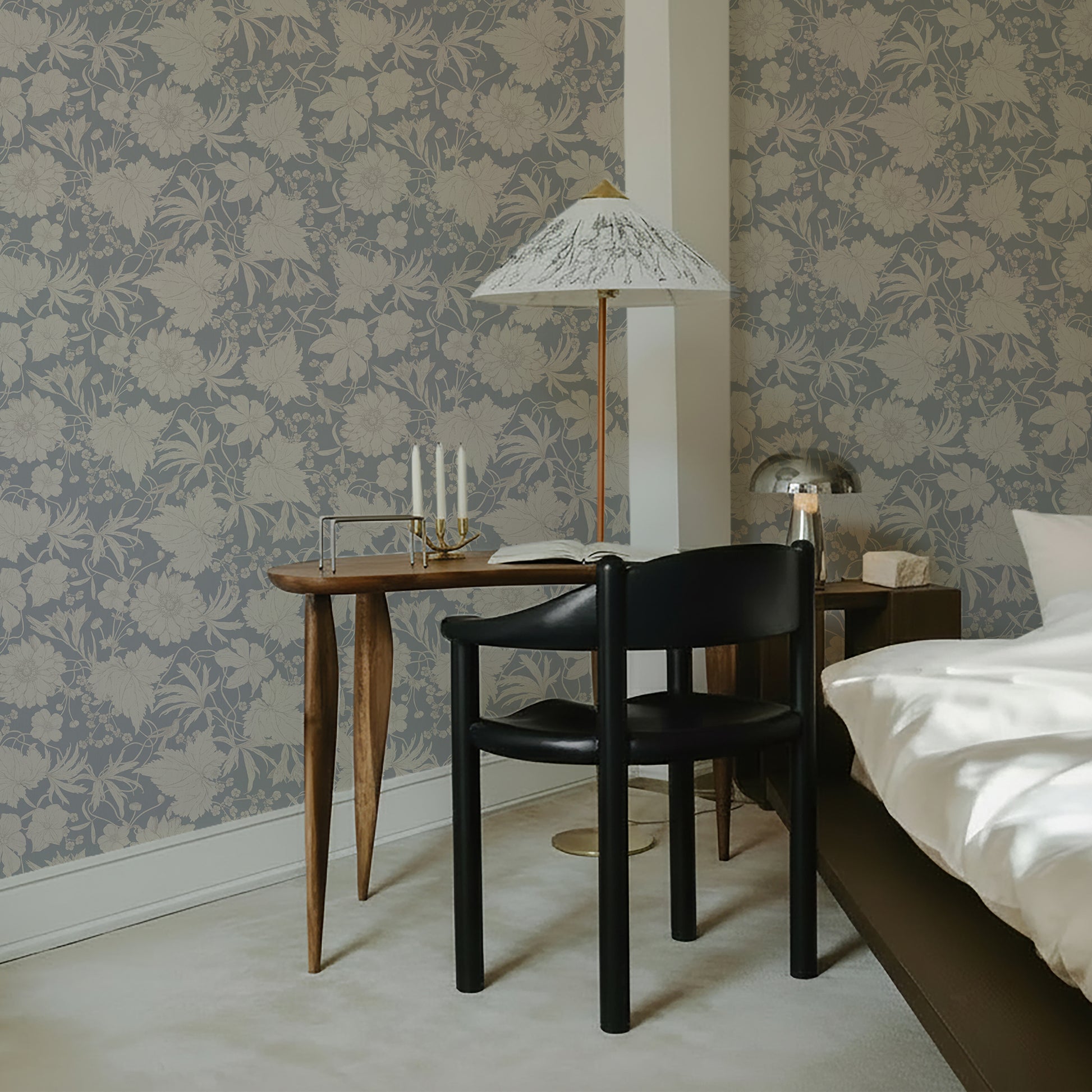 Modern bedroom with vintage modern timeless floral wallpaper with hummingbirds an subtle flowers, wooden table, black chair, and bed.