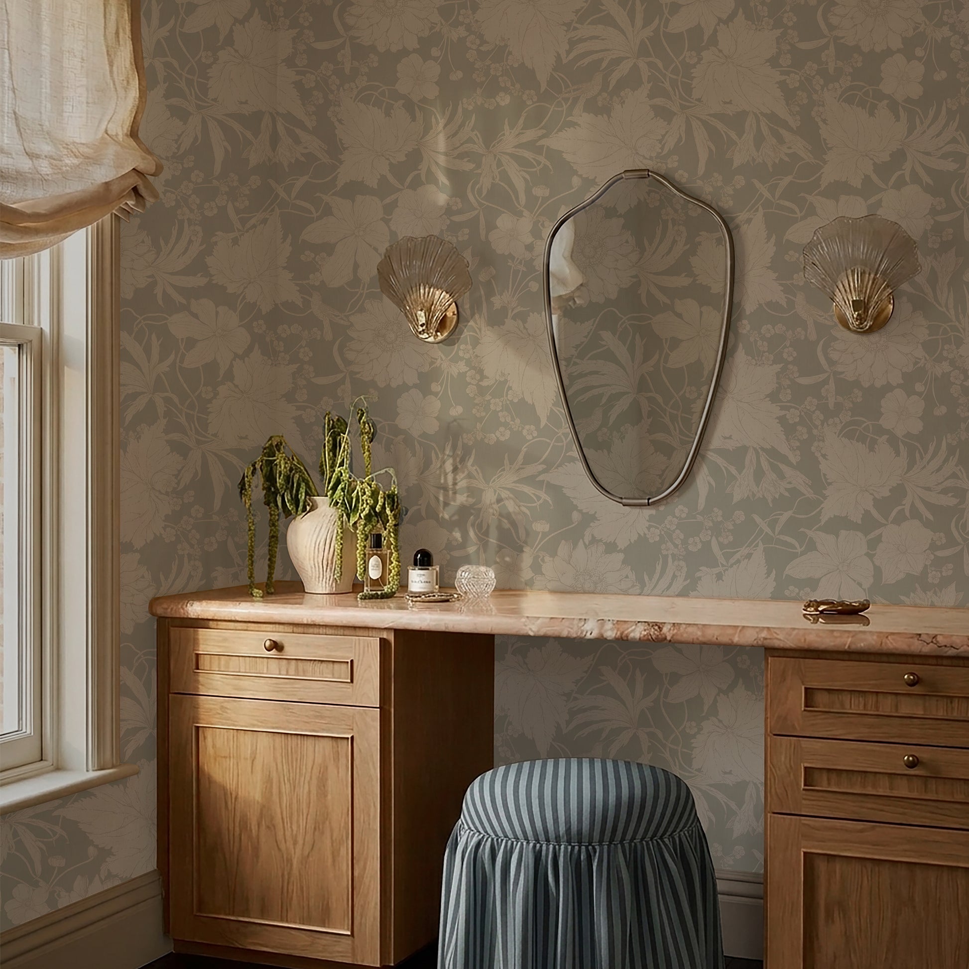 Wooden desk with decorative items against a sage green vintage style wallpaper with flowers, hummingbirds and leafs. 